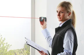 Aufmass nehmen - Decor-Union Service 124a Raumausstatterin misst mit einem professionellen Lasermessgerät das Fenster aus für Sichtschutz Sonnenschutz Gardine.
