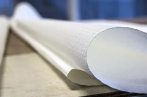 Verbrauchsberechnung - Nahaufnahme einer weißen Tapetenrolle, die auf einem Holztisch liegt. Glasfaster Raufaser